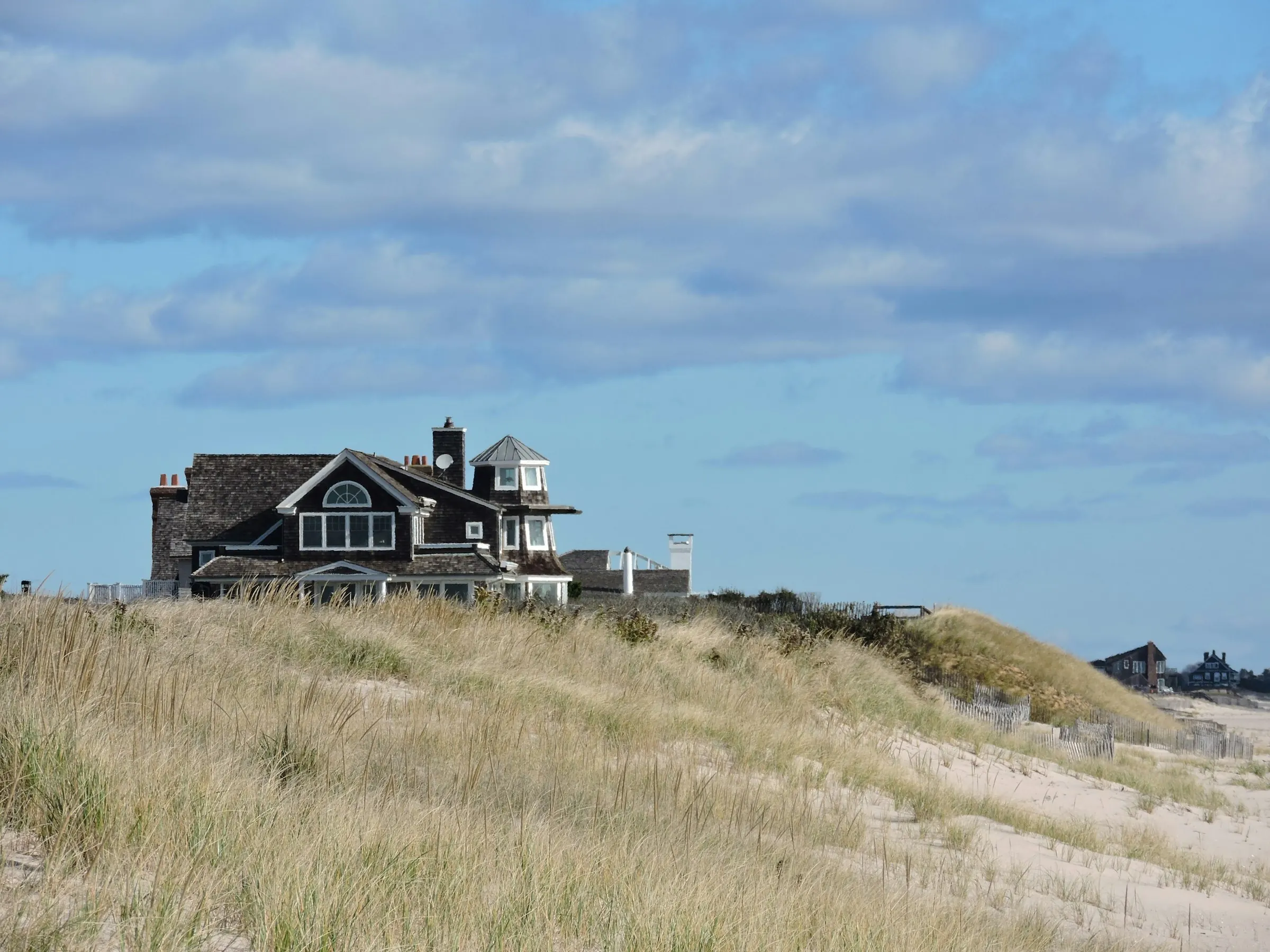 A shingled house on the dunes above the beach grass under a summer sky