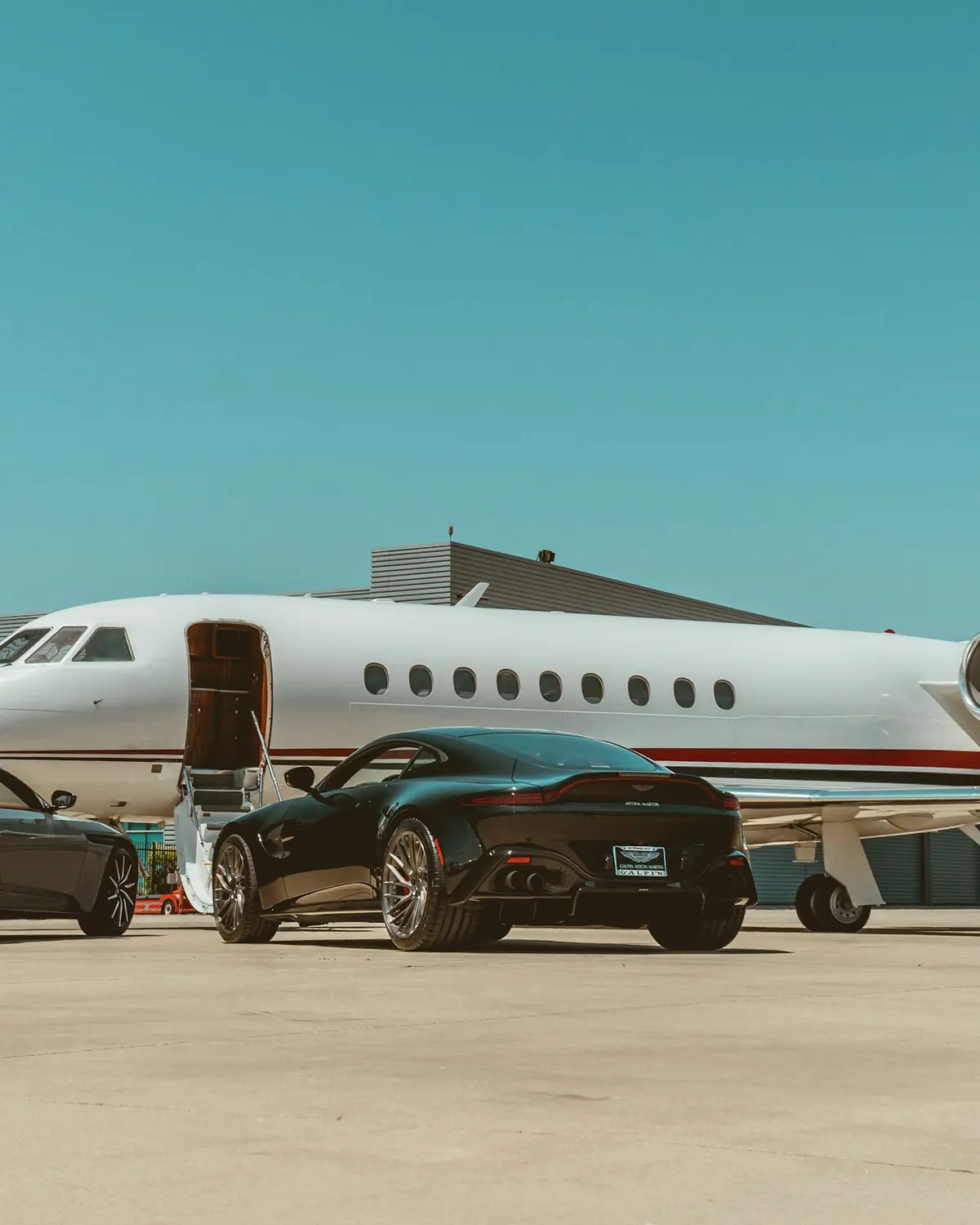 A private jet parked on a sunny ramp beside waiting cars